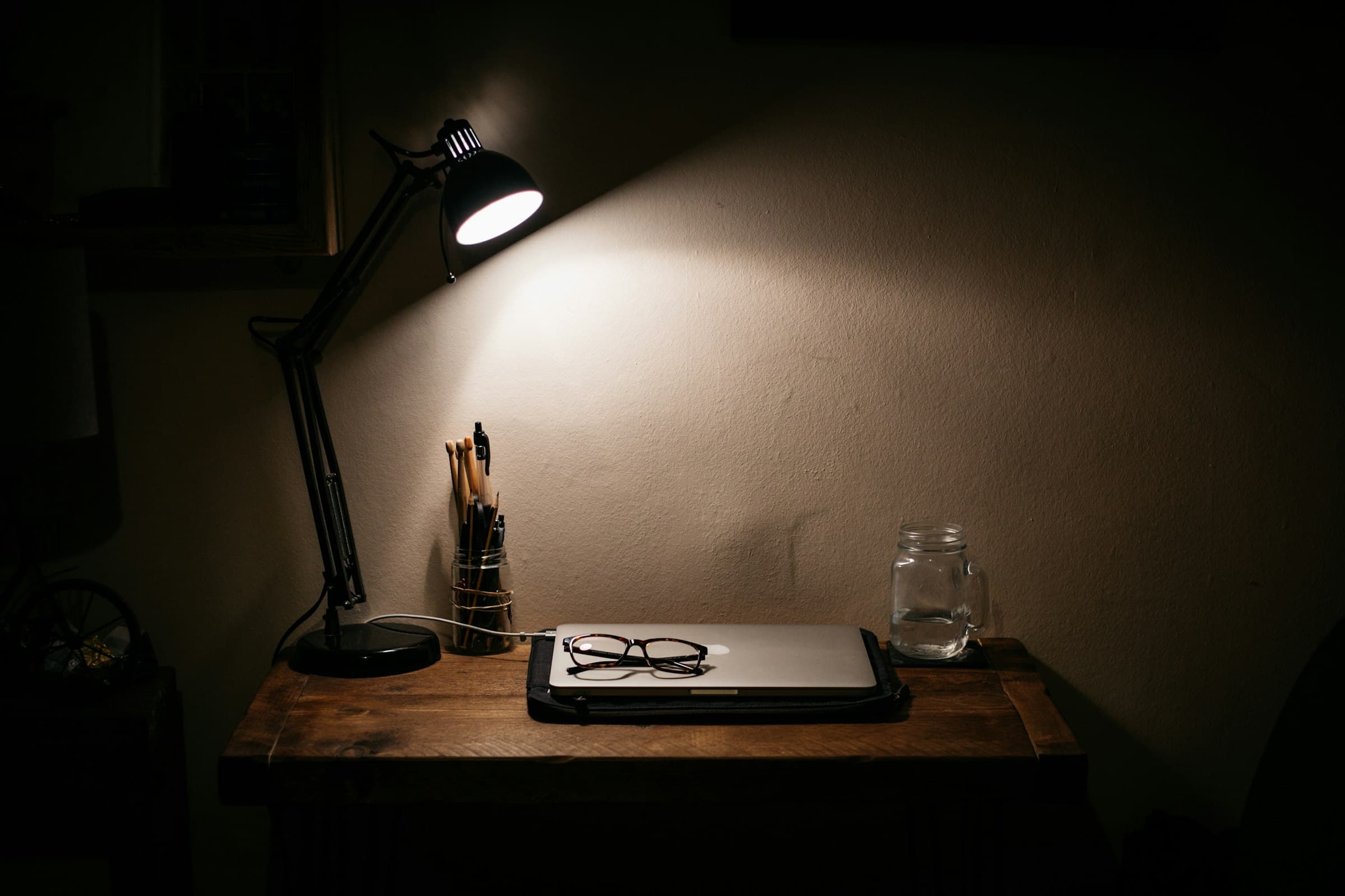 A desk lamp casting a warm pool of light over a wooden writing desk at night
